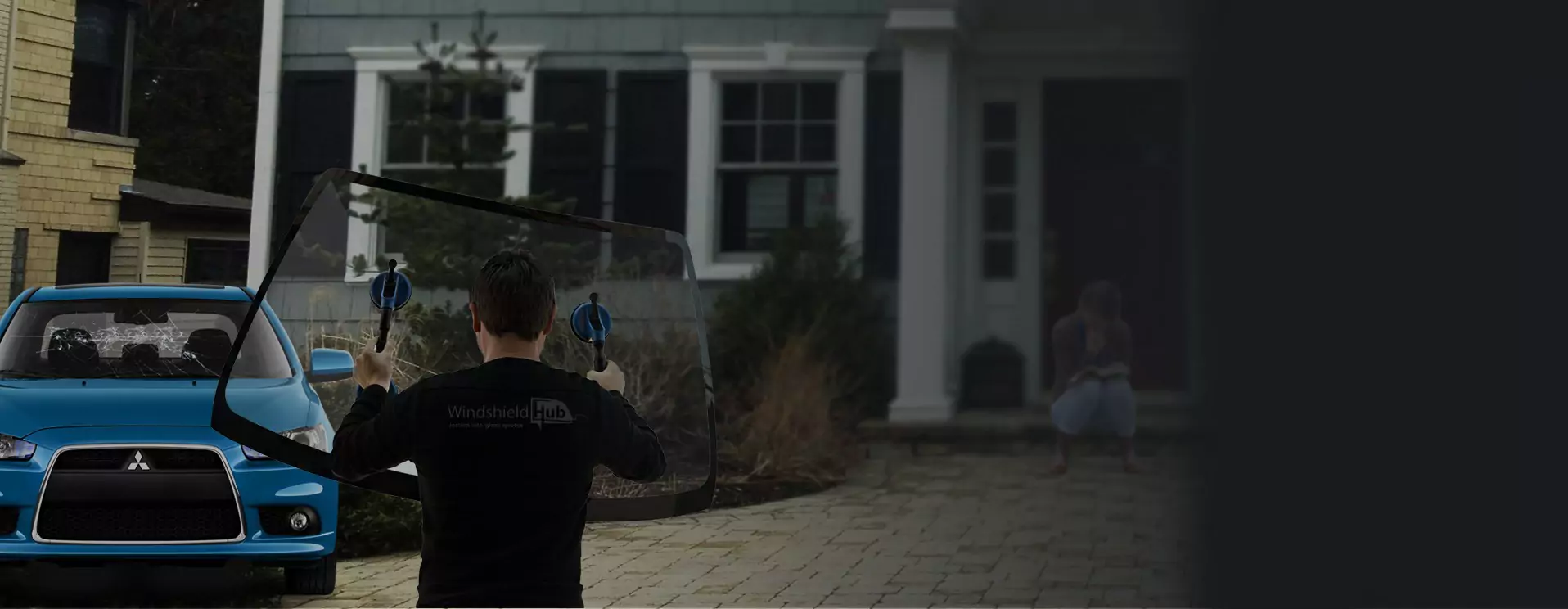 Man installing a car windshield with house and blue car in the background