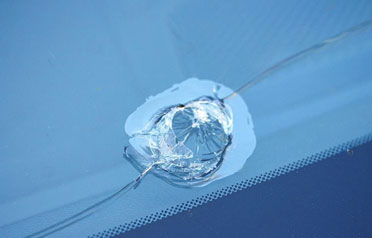 Large windshield crack with spiderweb damage spreading from impact point near the edge