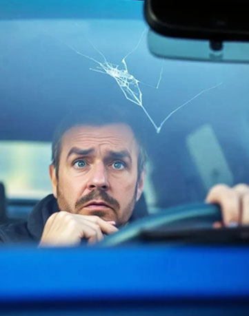 Worried driver looking at spiderweb windshield crack from inside blue car